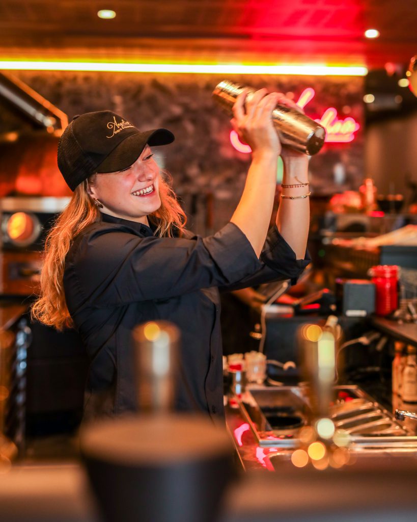 Au bar de la trattoria, préparation d’un cocktail au shaker sous les néons.
