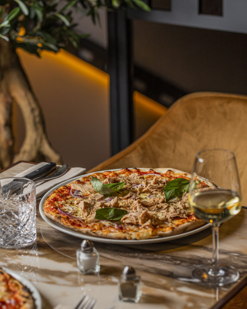 Une pizza pescatore sur une table de marbre, à côté d’un verre de vin blanc.